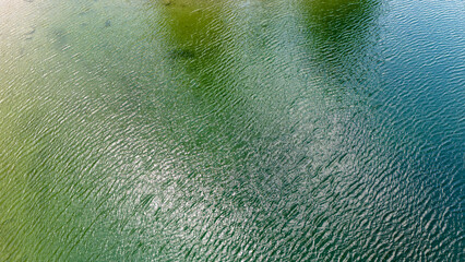 Aerial photo of green and dark blue water of an alpine lake in sunshine.