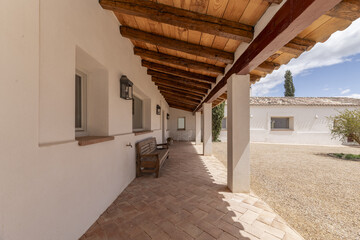 Covered porch with wooden roof of an Andalusian style country house with terracotta sidewalks,...