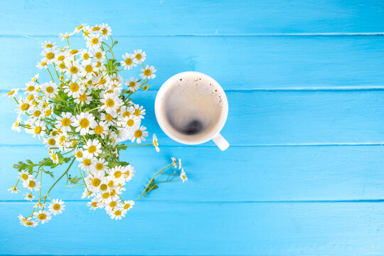 Chamomile daisy flowers bouquet, book, tea or coffee cup, relaxation holiday simple life enjoy summer background, on light blue wood background, top view copy space. Good day, good morning wishing