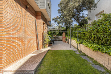 Perimeter garden with tiled path around a single-family house with brick facades and a metal pergola