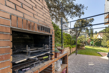 built-in barbecue with garden vines with a tiled path and a garden with grass in the background