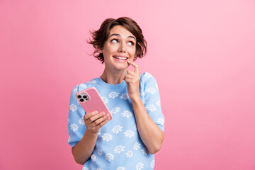 Portrait of creative pretty lady hold smart phone finger touch lips look empty space isolated on pink color background