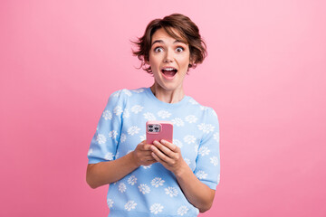 Portrait of astonished nice lady hold smart phone open mouth unbelievable isolated on pink color...