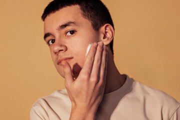 A close-up portrait of a teenage boy applying shaving foam to his cheek. A teenager is preparing to...