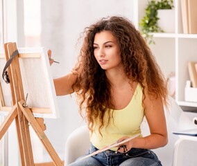 Beautiful girl painting picture on easel in light room