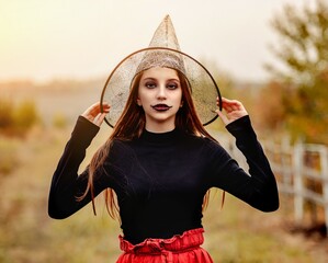 halloween portrait of teenage girl in witch hat smiling at camera on nature background