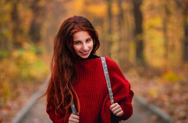 Young girl with backpack posing on colorful autumn park road