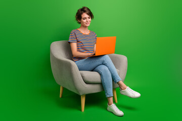 Full body portrait of nice positive lady sit cozy chair use wireless netbook isolated on green...
