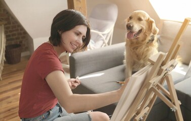Pretty girl artist drawing sketch with golden retriever dog using pencil and canvas. Beautiful...