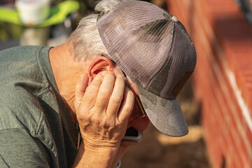 Senior man holding his ear while trying to talk and listen on his cell phone