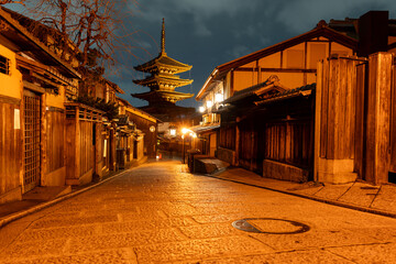 Yasaka Pagoda illuminated at night at the end of a street in the Gion District of Kyoto, Japan. City and pagoda are bathed in golden light.