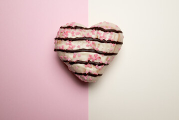 A heart-shaped donut with pink and white sprinkles on it. The sprinkles are arranged in a way that...