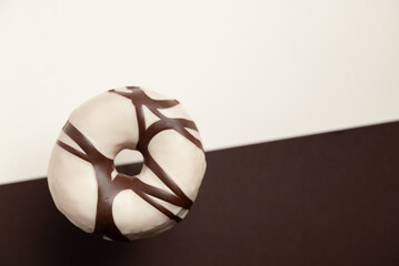 A donut with chocolate drizzle is suspended in midair on a black and white background. The contrast...