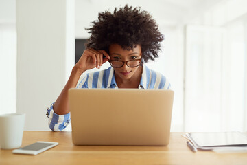 Woman, research and laptop at desk for blog, social media and networking in apartment. African female journalist, glasses and work from home for reading, newspaper article and online magazine
