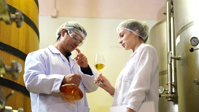 Winemaker woman with Caucasian man worker  wearing a sterile suit working and inspecting. Production line takes wine beverages out of aging tanks and puts them into bottles in a wine making factory.