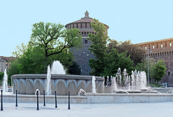 Piazza Castello big round fountain in front of Castello Sforzesco (Sforza Castle) in Milan, Italy, with blue sky