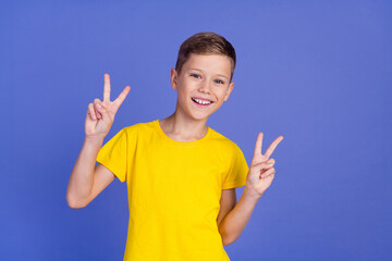 Photo of cheerful glad nice boy wear stylish yellow clothes showing v-sign symbol isolated on purple color background