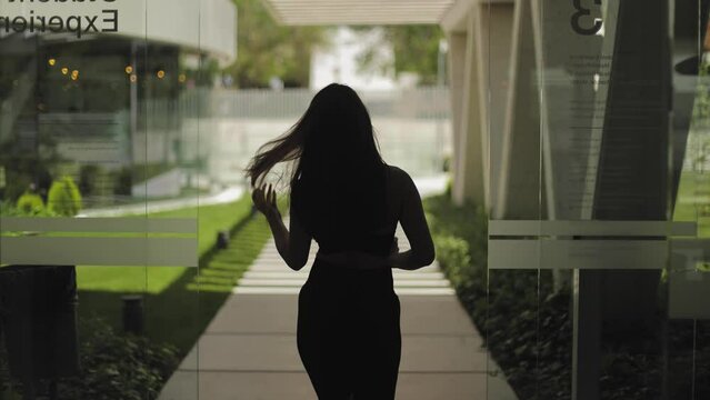 Athletic, attractive girl, model, view from the back, woman leaves an expensive, luxurious residential complex, exterior, life style and success, sun rays and shadows, cinematic frame