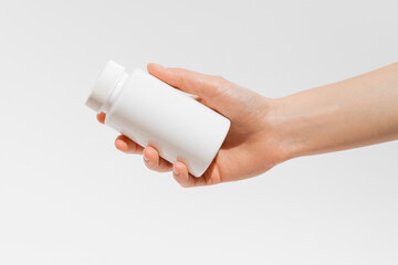 Female hand holding white pill jar mockup on white isolated background. Concept of pharmacy, natural dietary supplements, health care.