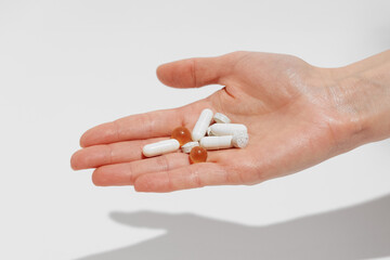 Female hand holding white pills and capsules on white isolated background. Concept of pharmacy, health, medicine, and dietary supplements. Image for your design