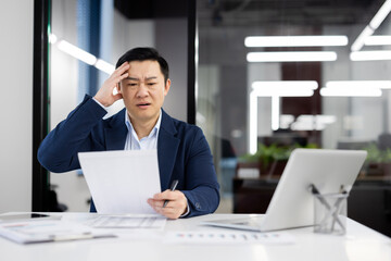 Frustrated korean boss of company grabbing head with hand while reading document in personal...