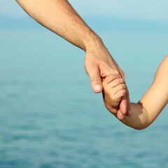 beautiful hands of parent and child by the sea - obrazy, fototapety, plakaty