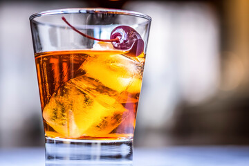 Closeup of an old Fashioned Whiskey Cocktail Drink with a cherry on top on the blurry background