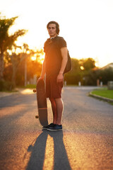 Portrait, man and skateboard in outdoor, street and backpack on headphones, summer and sunset. University student, physical activity and sports in urban, skater and athletic in edgy, exercise and fun © peopleimages.com