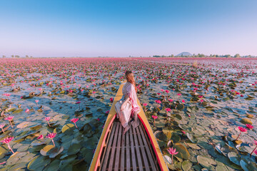 Young woman in Thai national costume sitting on a boat It is in a pink lotus pond.