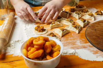 Women's hands mold triangle gomentashi cookies, a treat for the holiday of Purim, next to flour, a rolling pin