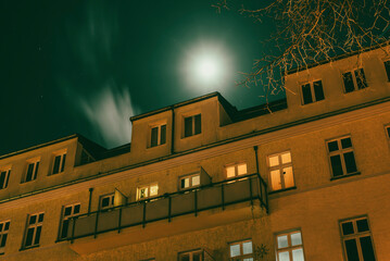 An apartment building photographed from below, with the moon in the background, long exposure,...