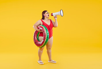 Full body photo of a funny fat overweight woman wearing red swimsuit holding rubber ring and speak in mouthpiece isolated on a studio yellow background. Summer holiday trip and vacation concept. - obrazy, fototapety, plakaty