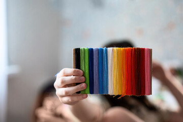 Child's hand holding a cardboard rectangle wrapped in rainbow-colored threads