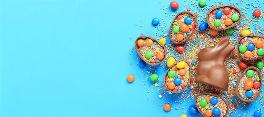 Chocolate bunny and eggs, candies, colored sugar sprinkles on a blue background, top view. Easter...