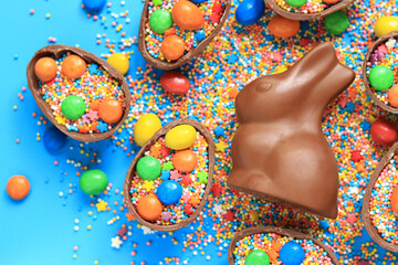Chocolate bunny and eggs, candies, colored sugar sprinkles on a blue background, top view. Easter...