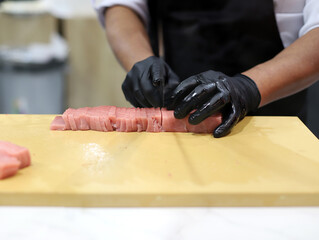 chef experto en sushi cortando atún para hacer sushis con un cuchillo en la tabla de cocina