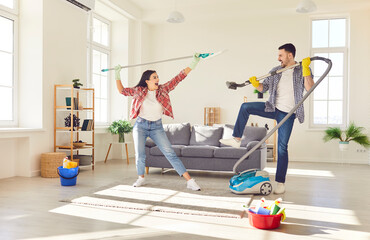 Happy couple tackles household chores and playing together with a mop and a vacuum, where cleaning...