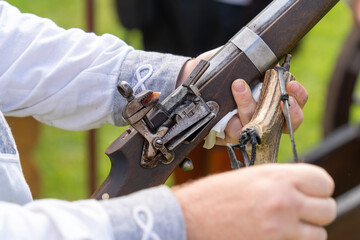 A medieval rifle with a flint firing mechanism and a bone powder holder in a man's hand