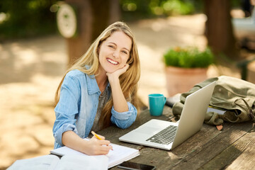 Female student, laptop and writing in portrait, smile and study with coffee, thinking and outdoor...