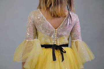 Close-up of a child s yellow princess dress with pearl buttons and a velvet ribbon, showcasing...