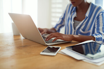 Laptop, woman and hands typing at desk for blog, social media and email in apartment. African female journalist, technology and work from home for research, newspaper article and online magazine
