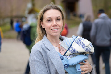 Portrait of a happy woman looking to camera while holding and carrying it in a baby carrier