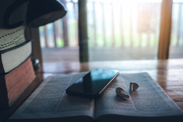 Bible and a smartphone with earphones on wooden table, Christian online technology concept, online live church for sunday service. holy bible book and online study.