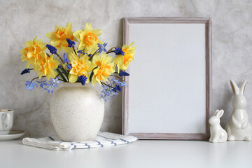 Easter background with an empty frame and figures of Easter bunnies on the table. daffodils.