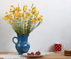 a rural still life, a bouquet of yellow daisies and red strawberries. a polka dot mug.