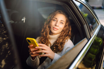 Young woman sits in the back seat of a car and talks on the phone. The concept of business, technology, travel, online communication. Taxi.