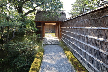 A Japanese scene : a gate with a thatched roof and a thatched wall.