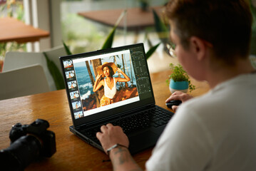 Photographer edits model photo on laptop at cafe table. Freelancer works on image processing, uses...
