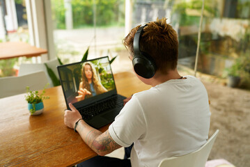 Gen Z individual with tattoos telecommutes from cafe, engaging in video call on laptop while...