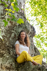 Beautiful woman with gorgeous curly hair doing yoga in nature, dressed in white and yellow combination, concept: active healthy life, in love with nature, support, balance, wellbeing, energy